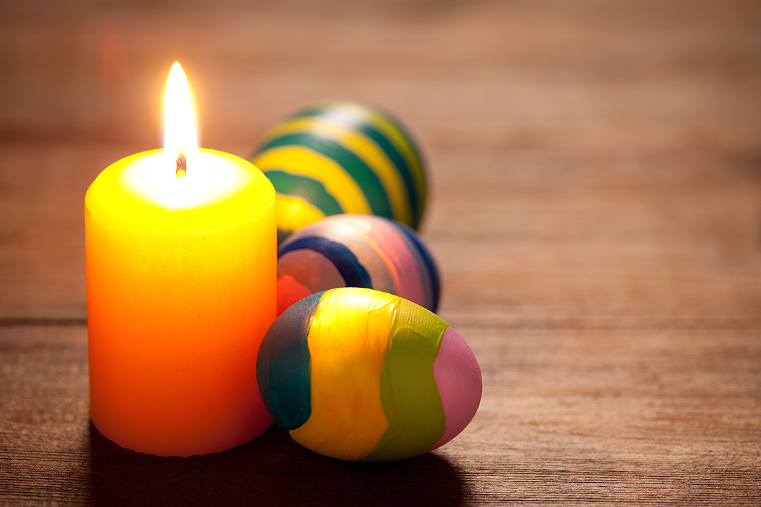 Colorful easter eggs and candle on old wooden table